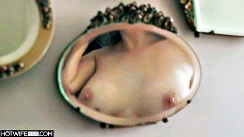 Mirror reflection of young fair-skinned woman's bare small tits with pink nipples fully exposed.