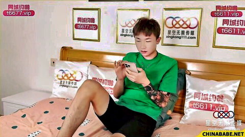 Young Asian man in green shirt and shorts sits on bed checking phone, Fuck My Wife scene