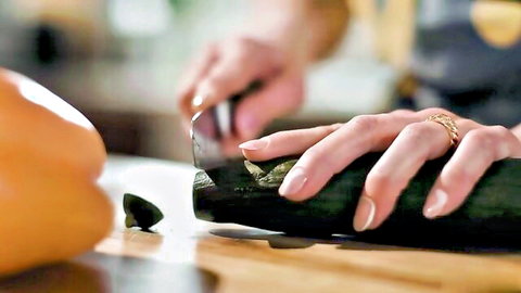 Manicured hands slicing thick green zucchini and orange bell pepper on wooden board