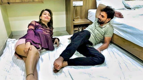 Seductive South Asian brunette in purple lace top and shorts lounges with man on hotel bed