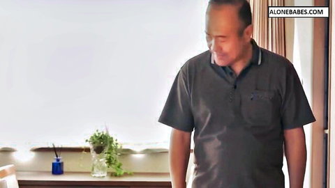 Mature smiling Asian man in polo shirt standing by window in cozy room