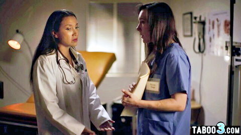 Asian doctor in white coat seduces brunette nurse holding clipboard in exam room