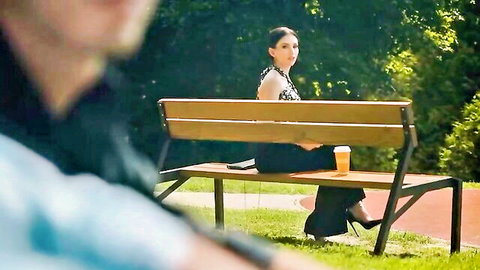 Brunette in short black skirt and high heels sits on park bench holding coffee cup with man watching