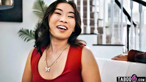Smiling petite Asian teen in red tank top with butterfly necklace on couch for taboo fun