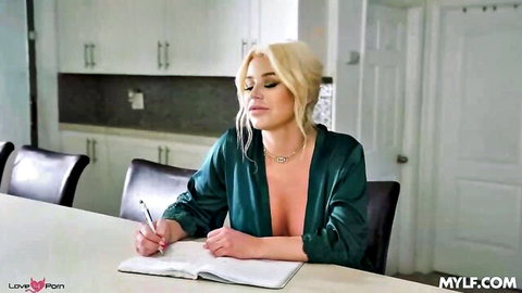 Blonde MILF with huge tits spilling from low-cut satin blouse writing at kitchen table