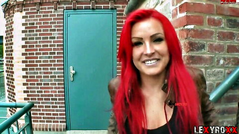 Busty redhead with big tits smiling teasingly outdoors in leather jacket and cleavage top
