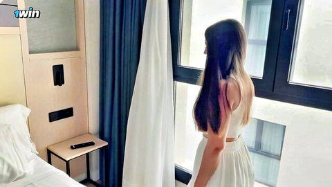 Brunette in white crop top and skirt by hotel window, teasing side view