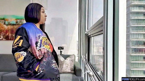 Busty ebony babe in sexy Lakers jacket stands by hotel window overlooking LA skyline
