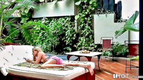 Topless blonde with huge tits lounges on outdoor couch in pink thong holding phone