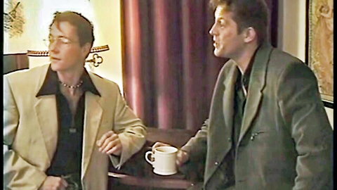 Two suited men intimately chatting over teacups in luxurious red room