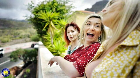 Three mature women in colorful dresses laughing on sunny outdoor terrace