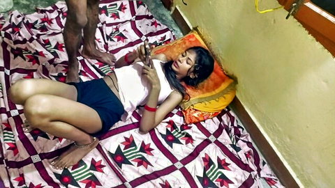 Indian step-sis in shorts lies on bed, legs spread, checking phone teasingly
