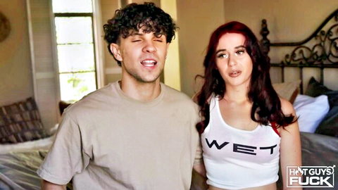 Curly-haired guy in tee and redhead babe in tight wet tank top smiling in bedroom