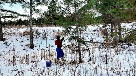Curvy blonde woman in tight skirt cutting Christmas tree in snowy outdoor forest