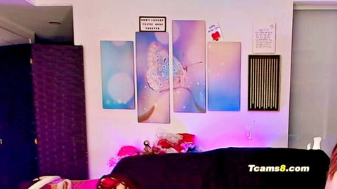 Horny TS girl in purple-lit cam room with butterfly art, ready for shemale fun