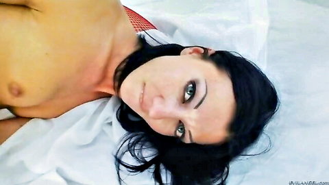 Topless brunette MILF with green eyes and perky tits lying seductively on white sheets