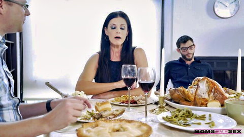 Brunette MILF mom sits seriously at Thanksgiving dinner table with turkey, wine, and family