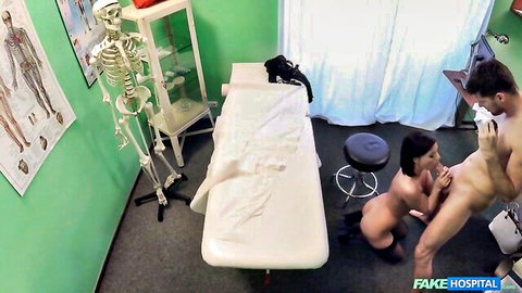 Skinny brunette in stockings kneels giving blowjob to nude man's hard cock in hospital room