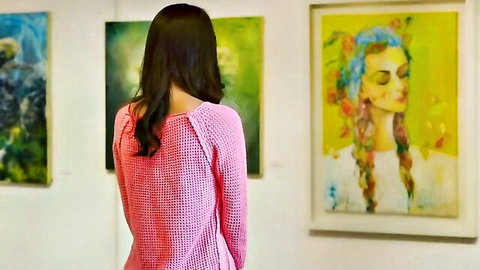 Sexy East Asian woman in sheer pink knit sweater viewing art gallery paintings from behind