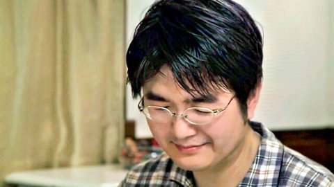 Close-up of smiling Japanese man with glasses, black hair and plaid shirt collar
