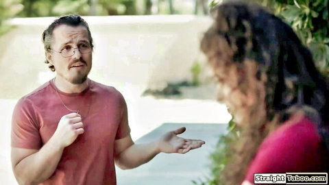 Glasses-wearing man in red shirt gestures to long curly-haired brunette woman in pink top outdoors