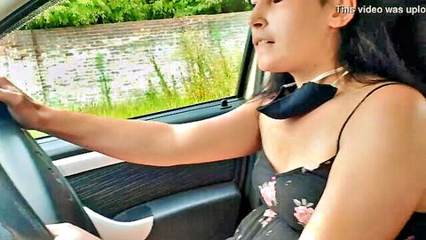 Asian woman in floral dress driving car, teasing while masked