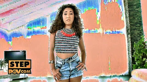 Curly-haired brunette babe posing seductively in fringed crop top and tight denim shorts