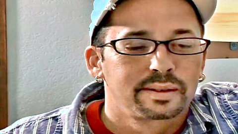 Close-up portrait of mature man with glasses, goatee, earrings, and backward baseball cap
