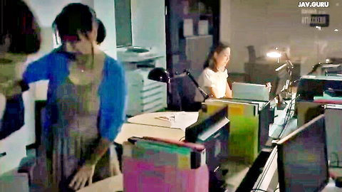 Two Asian women in skirts and cardigans at office desks with monitors and files in JAV scene