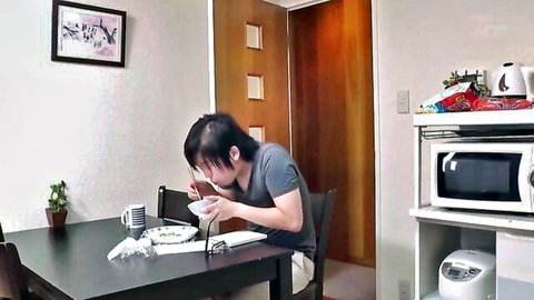 Emo Japanese guy slurping noodles from bowl at kitchen table