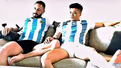 Two muscular men in Argentina soccer jerseys relaxing intimately on couch