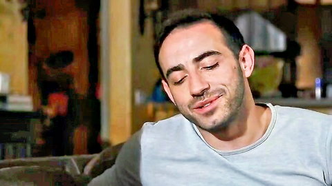 Handsome stepbrother smiling on couch in casual gray shirt, teasing vibe