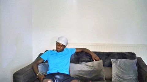 Hot black stud lounging relaxed in tight leather shorts and blue tee on velvet couch