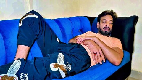Bearded man lounging relaxed on blue couch in sweatpants and sneakers