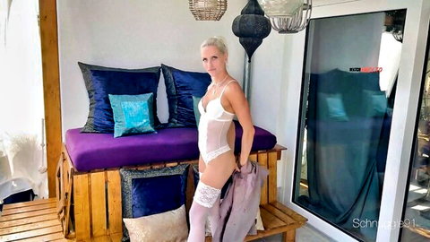 Skinny blonde in sheer white lace bodysuit and garter stockings poses seductively on balcony