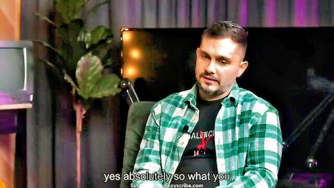 Bearded man in checkered shirt sits in studio interview with plants and neon lights