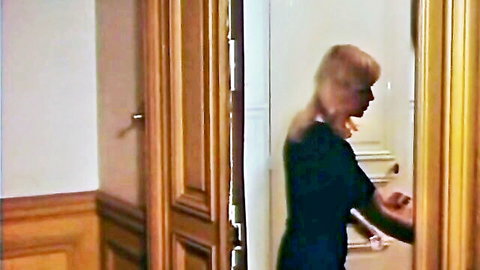 Blonde woman in black dress opening ornate wooden door in vintage hallway