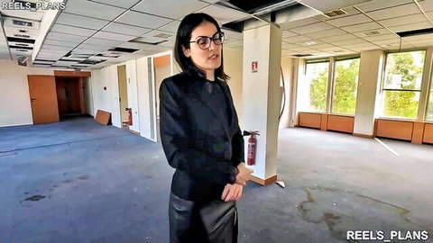 Sexy glasses-wearing businesswoman in tight leather skirt stands in empty office