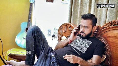 Handsome South Asian Indian man lounging on sofa talking on phone in jeans and t-shirt