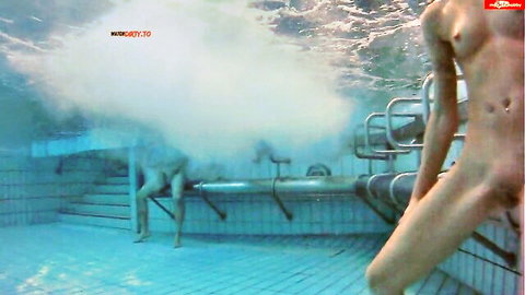 Naked man with visible flaccid cock standing underwater in tiled pool amid rising bubbles