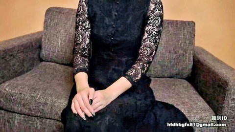 Sensual woman in black lace dress sits teasingly on couch with painted nails