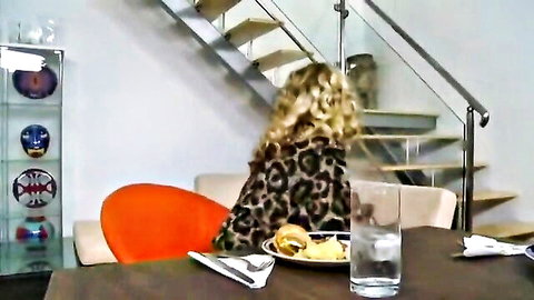 Blonde woman in leopard print dress sits at table eating burger and fries