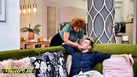 Mature redhead massages young guy's neck on sofa in modern kitchen