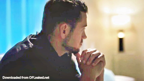 Handsome bearded man in profile view with hands clasped under chin in dimly lit room