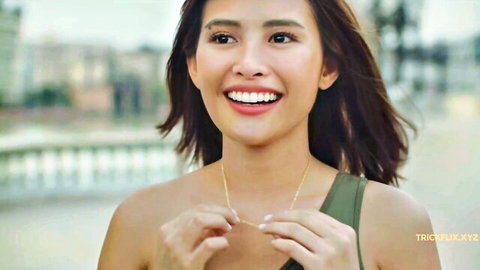 Smiling Asian dance instructor in green top holding gold necklace outdoors