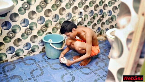 Shirtless young Indian boy squats in colorful bathroom dipping cloth in blue bucket