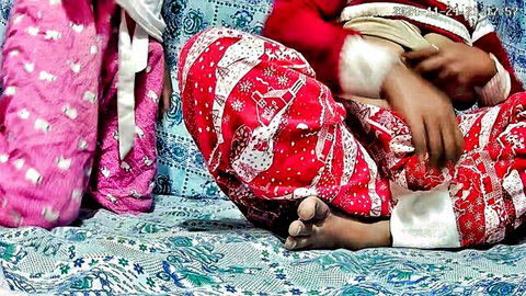 South Asian girl in red Santa pajamas sits on bed showing dirty bare foot soles