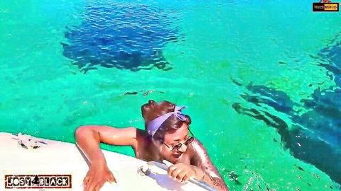 Shirtless tattooed man in sunglasses and headband dives into turquoise water from boat
