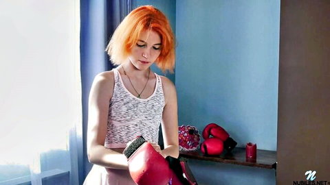 Redhead Lissa Fox in white tank top and pink skirt holding boxing gloves