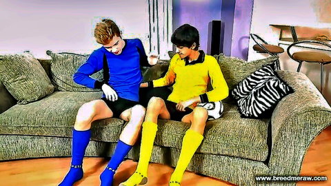 Two cute gay soccer boys in blue and yellow uniforms sit spread-legged teasing on couch